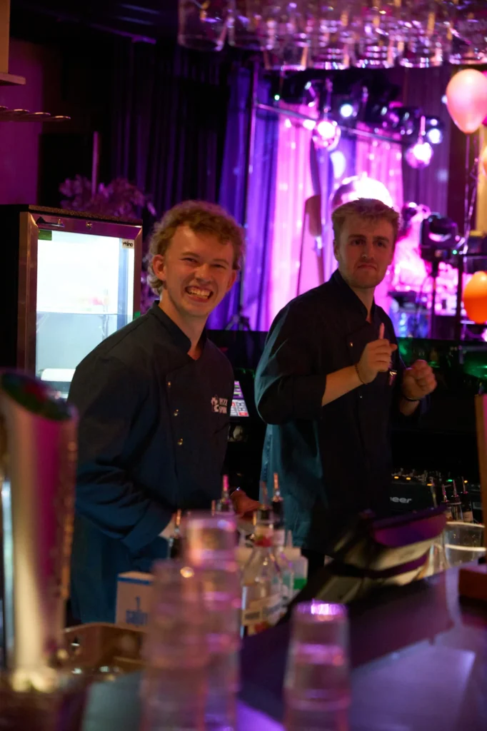 Emil, med krøllede hår og Marius fra Puzzle Spiritz står og smiler. Marius danser.