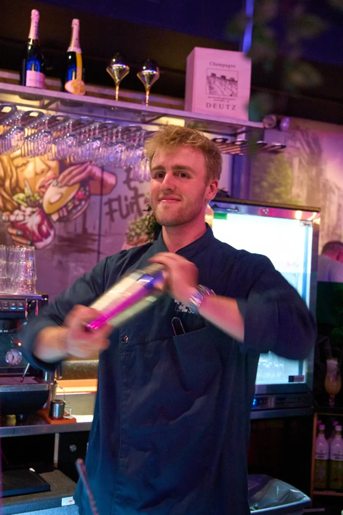 Marius fra Puzzle Spiritz står og smiler med en shaker i hånden, i pink lys.