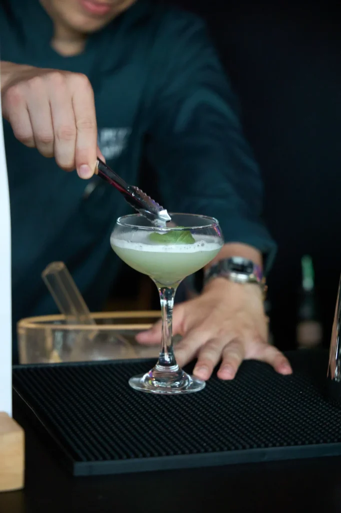 Billede af et stykke garnish, bliver placeres på en grøn martini drink.